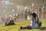 A woman in a summer dress takes a long swig from a can in front of a crowd of people at a music festival.