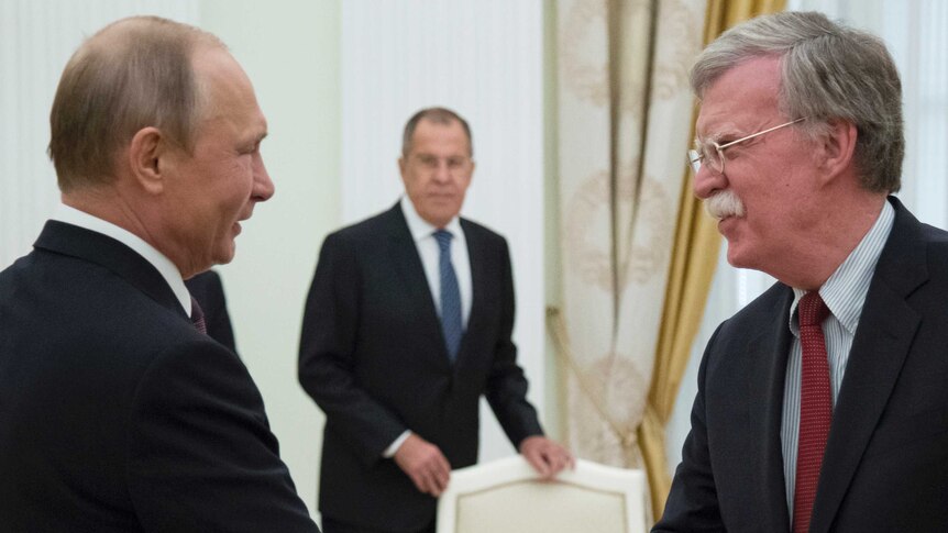 Mr Putin and Mr Bolton smile and shake hands, with Russian Foreign Minister Sergei Lavrov in the background