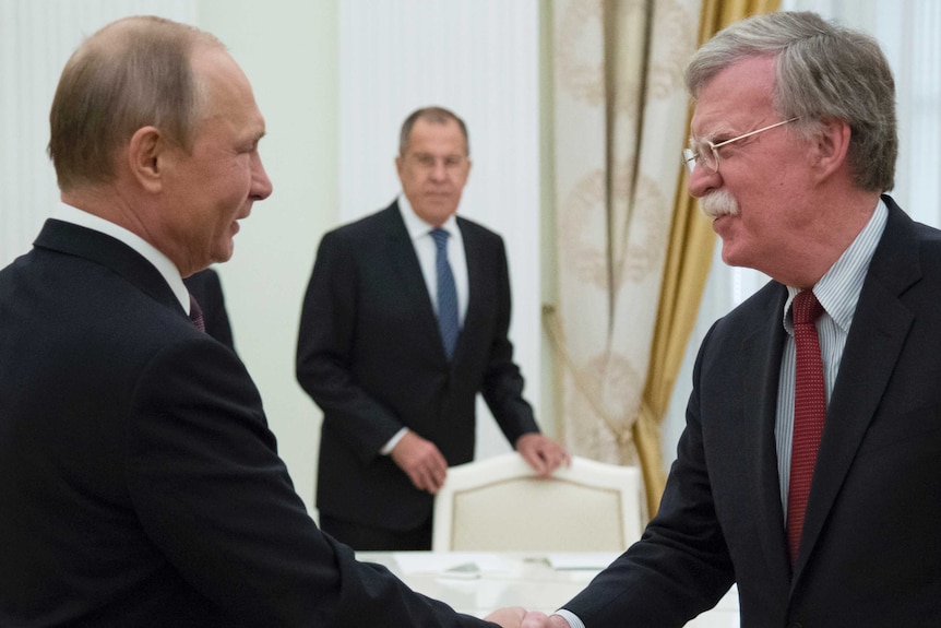 Mr Putin and Mr Bolton smile and shake hands, with Russian Foreign Minister Sergei Lavrov in the background