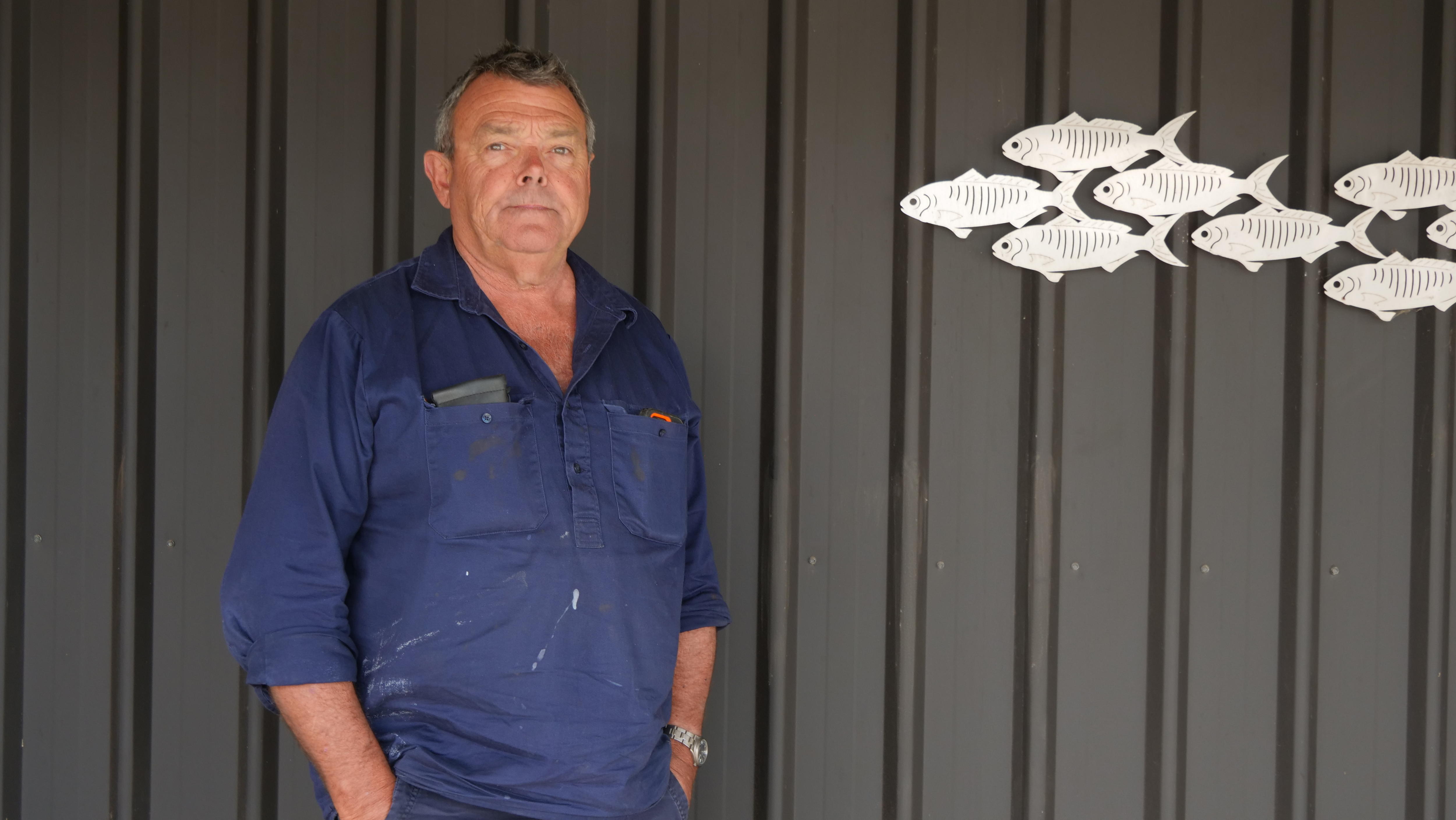 Plano médio de um homem parado ao lado de um peixe de metal.