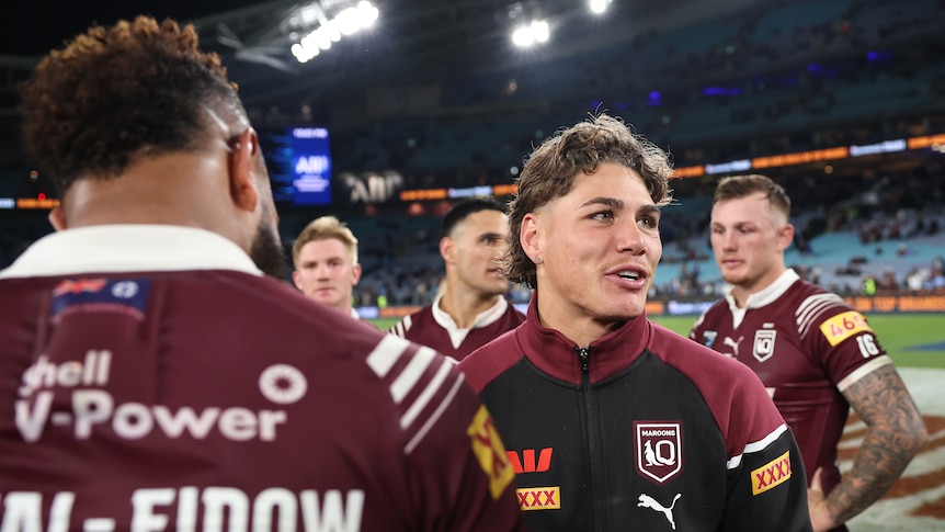 An injured Queensland State of Origin stands around his teammates after a game.
