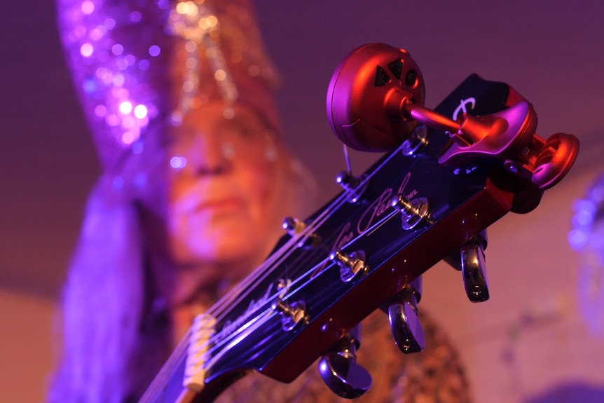 Face of woman with long hair playing guitar under bright coloured lights.