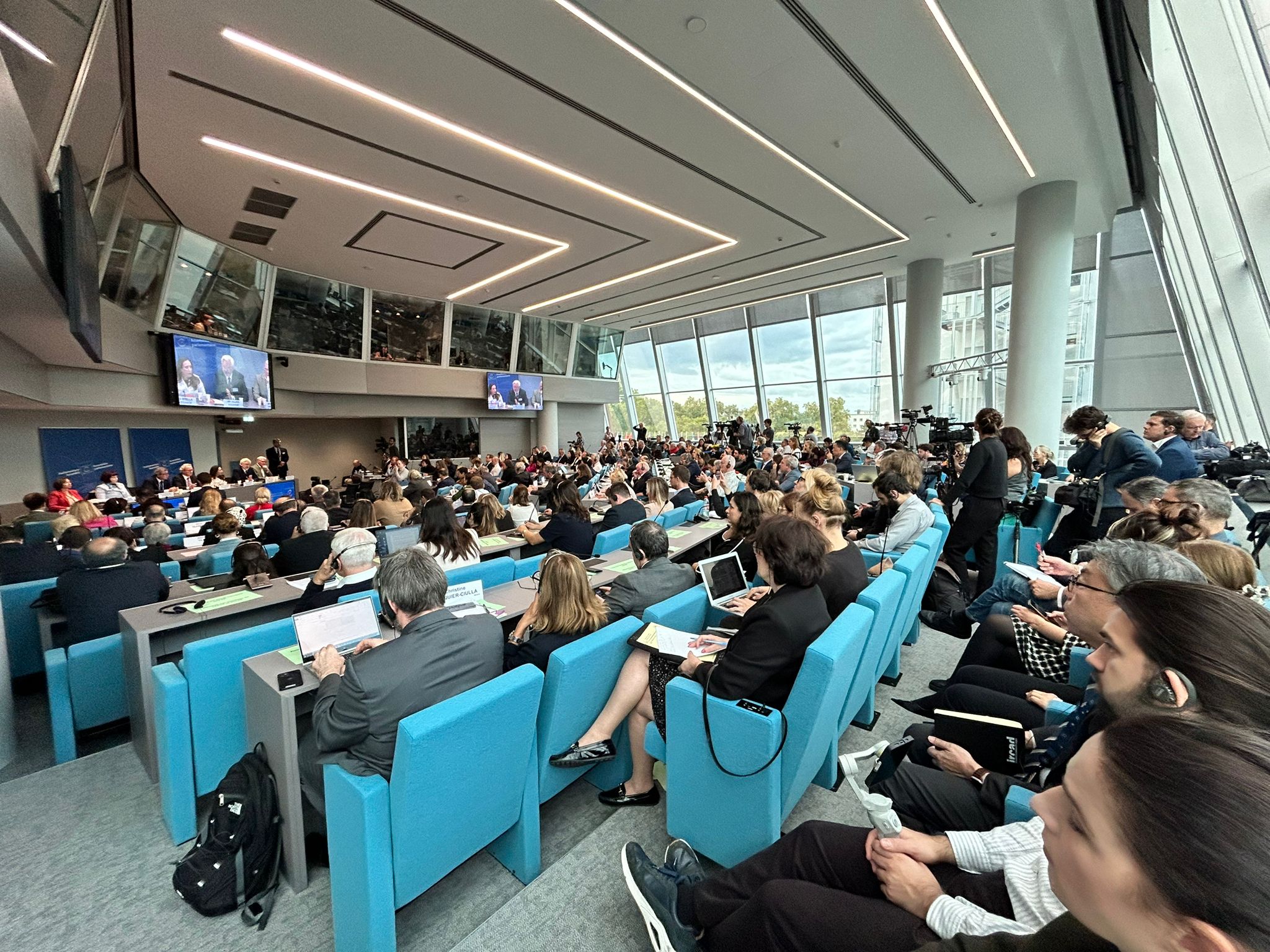 A crowd sits watching a row of speakers. 