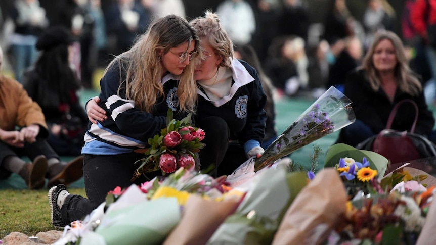 Two women are seen laying flowers at a vigil for Eurydice Dixon.