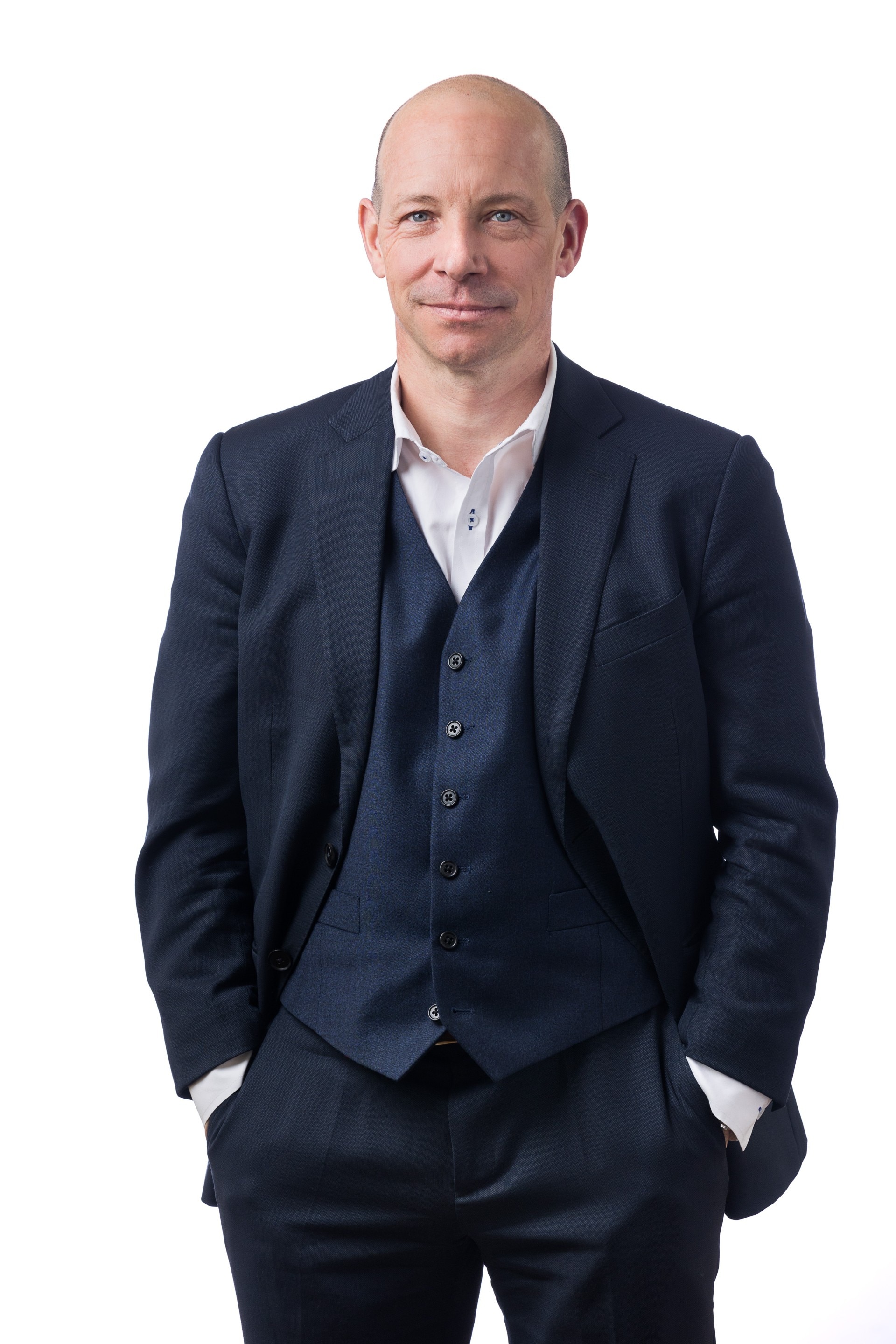 Um homem vestido com uma suíte azul e camisa branca olha para a câmera.