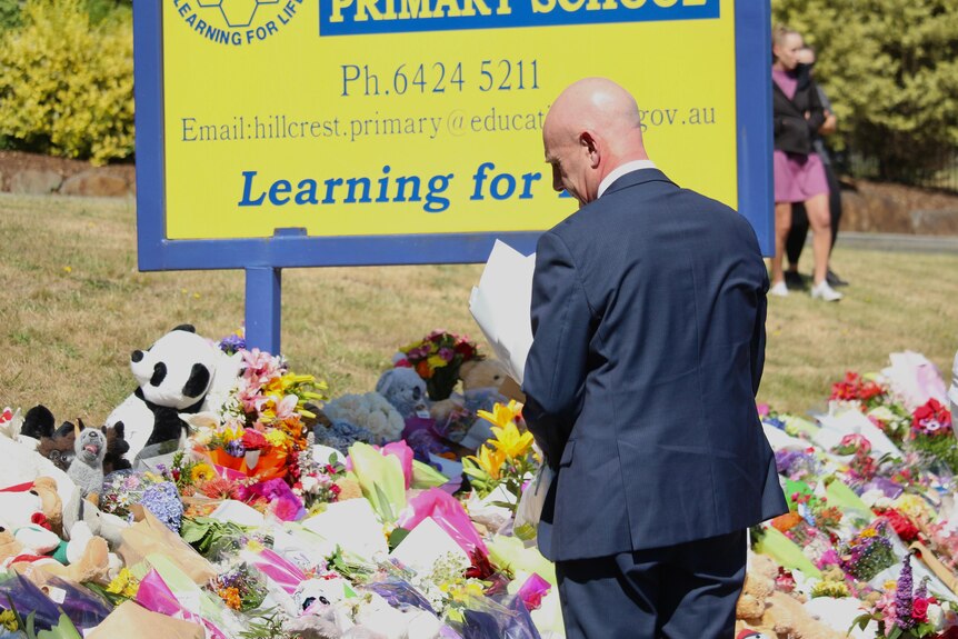 Tasmanian Premier Peter Gutwein places flowers outside school near a sign for the school where other flowers and toys