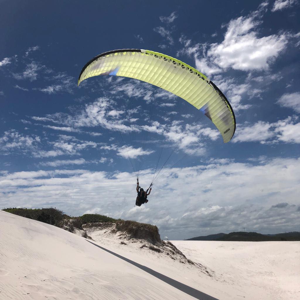 paraglider over sandy beach dunes