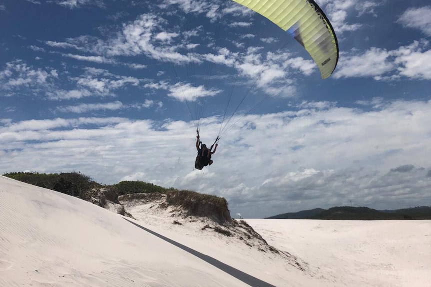 paraglider over sandy beach dunes