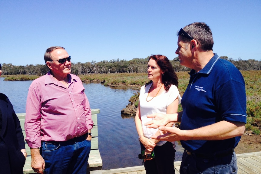 A woman with shoulder length red hair stands on a jetty talking to two men.