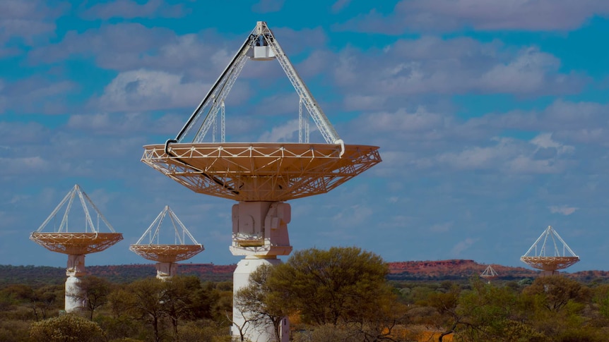 Four radio telescopes stand in an outback plain.