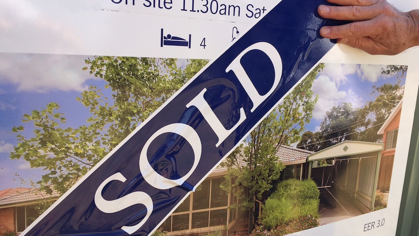 A sold sticker is placed over an auction sign for a house.