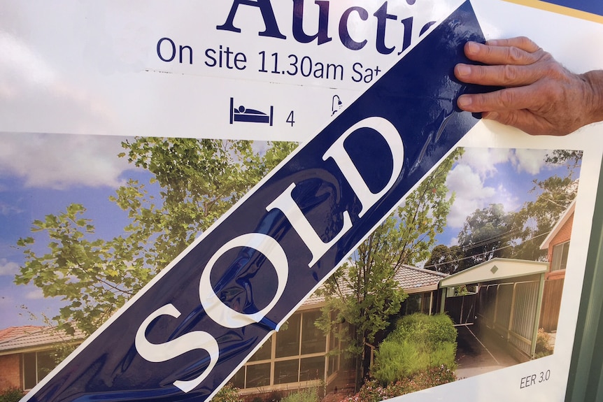 A real estate sign for a house auction with a sold sticker pasted across the front.