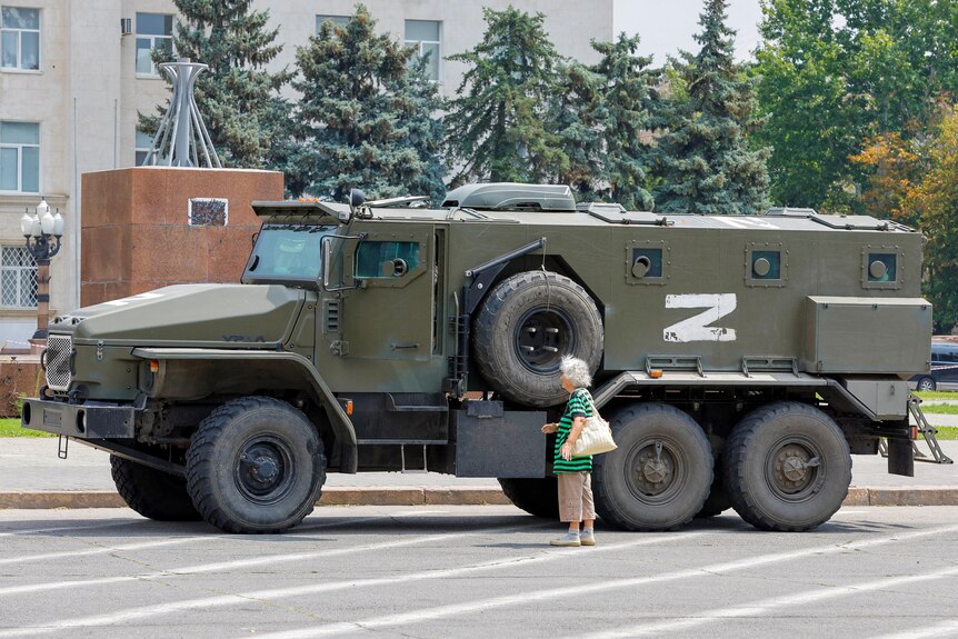 A woman stands next to a Russian forces truck. 