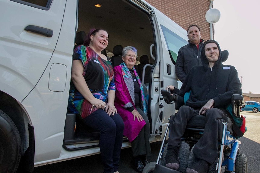 A man in a wheelchair near a van with two women sitting in it and a man standing
