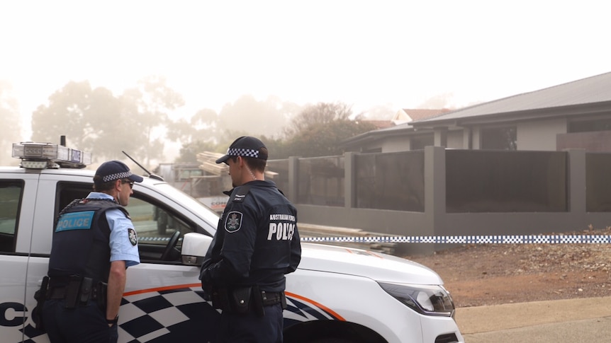 Two AFP officers stand next to a police car outside a house on a foggy morning.