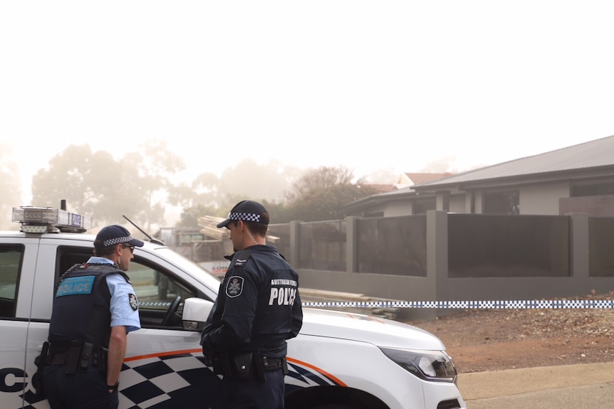 Two AFP officers stand next to a police car outside a house on a foggy morning.