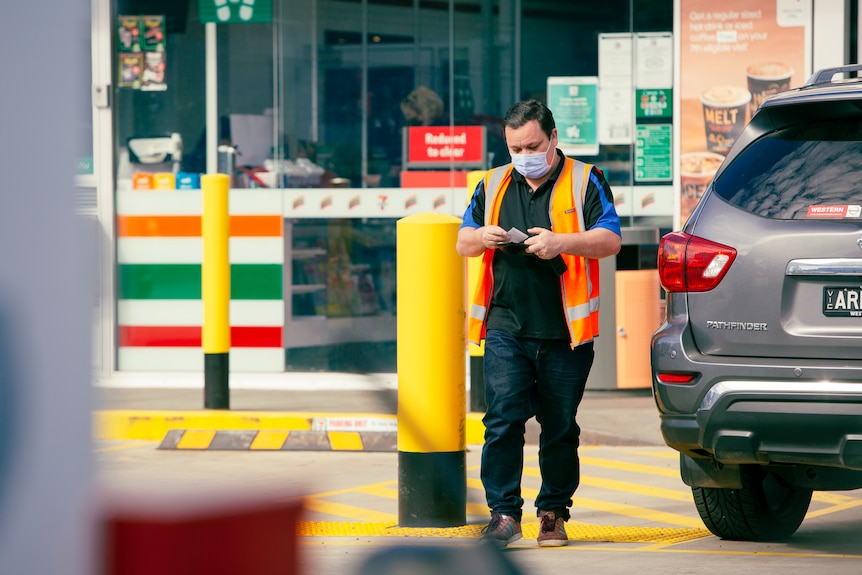 A man in an orange high-vis vest looks at a receipt in his hand after leaving a petrol station.