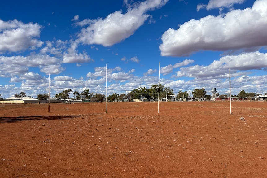 Football goal posts against a red dirt oval and deep blue sky.