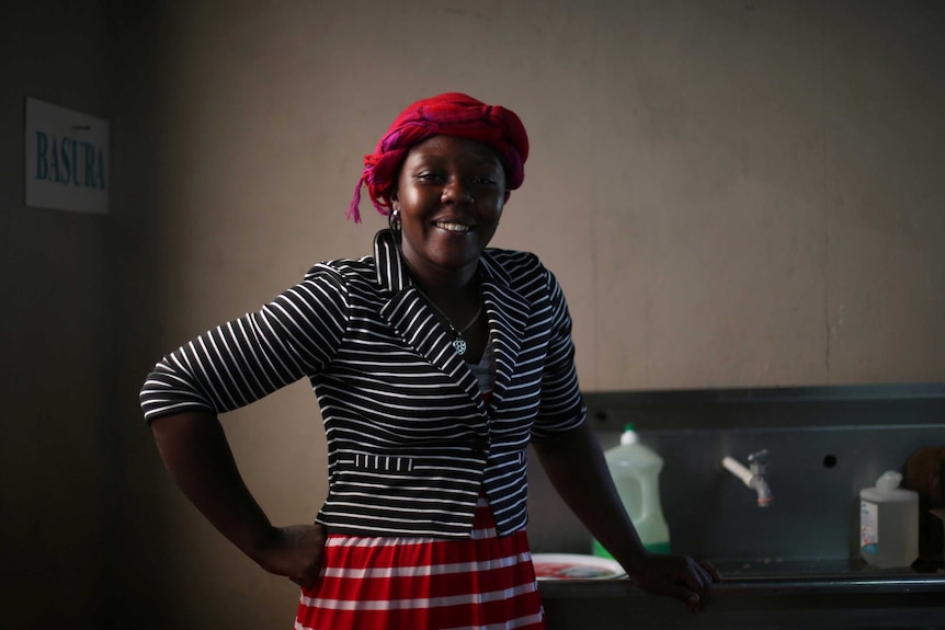 Naomi Josil, a haitian refugee, wears a red head piece and poses for a photo with her hand on her hip.