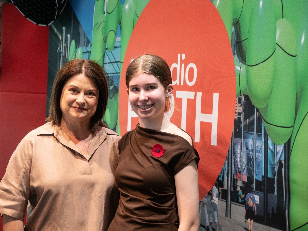 An older woman Nadia Mitsopoulos stands next to a younger woman Amalia Cailes in a radio studio