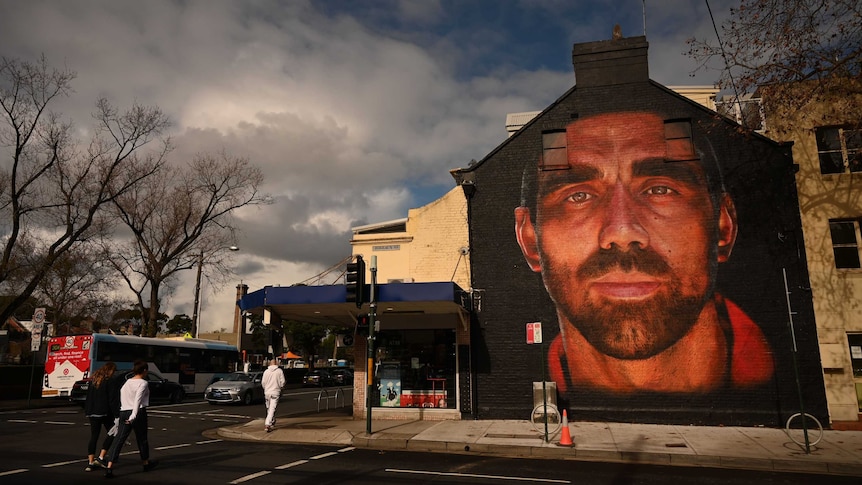 Pedestrians walk past a mural of the face of footballer Adam Goodes painted on the side of a terrace house