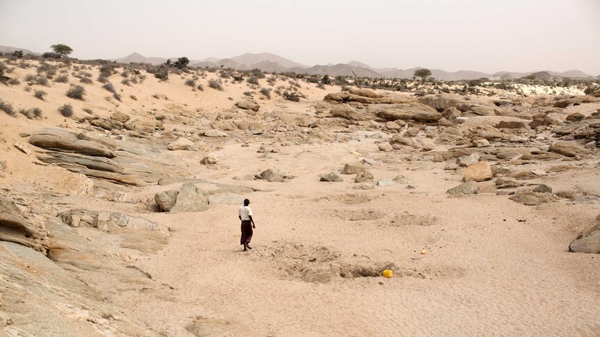 man walking near hole in a sandy, rocky landscape.