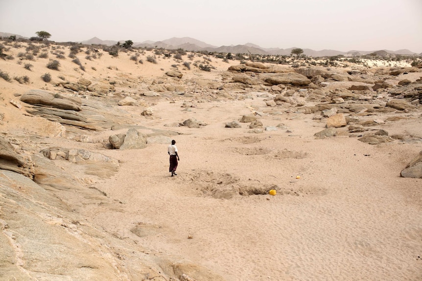 man walking near hole in a sandy, rocky landscape.