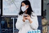 A woman wearing a face mask waits at a Melbourne tram stop.