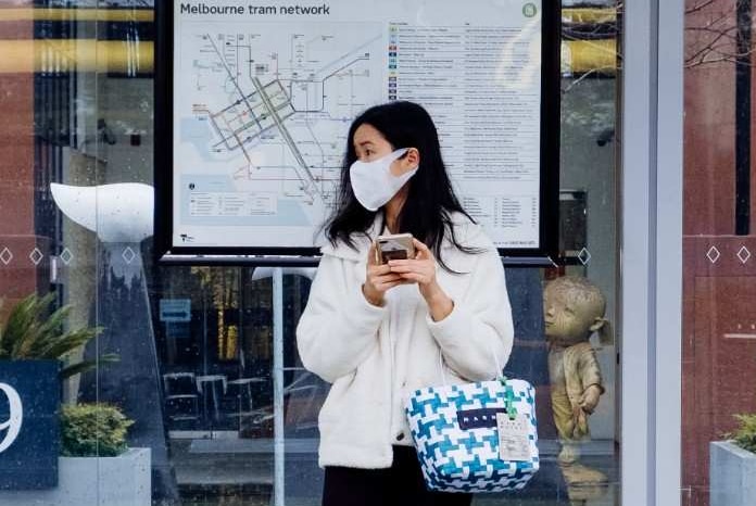 A woman wearing a face mask waits at a Melbourne tram stop.
