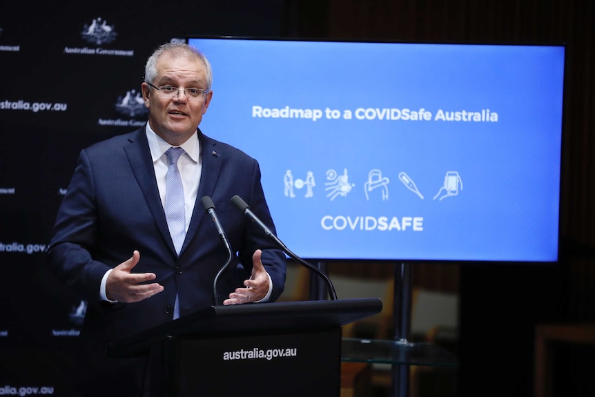 Australian Prime Minister Scott Morrison stands in front of a projector screen that says Roadmap to a COVIDSafe Australia