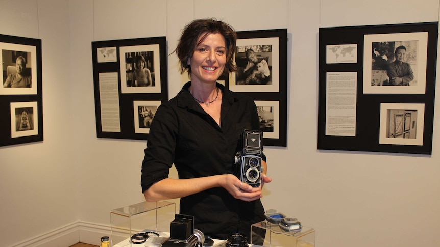A lady stands in an a photographic exhibition holding a an old film camera
