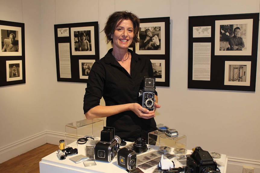 A lady stands in an a photographic exhibition holding a an old film camera