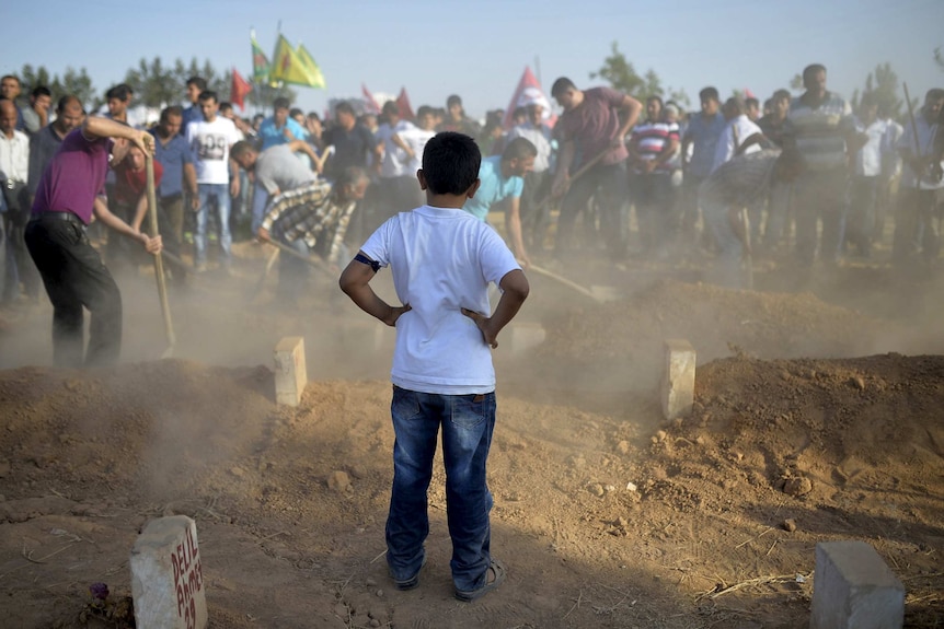 Boy watches graves prepared for 32 people killed in an attack on a Kurdish cultural centre