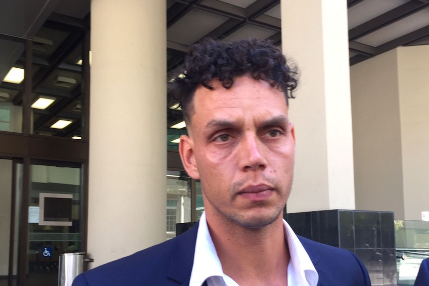 A man in a suit without a tie outside a courthouse.