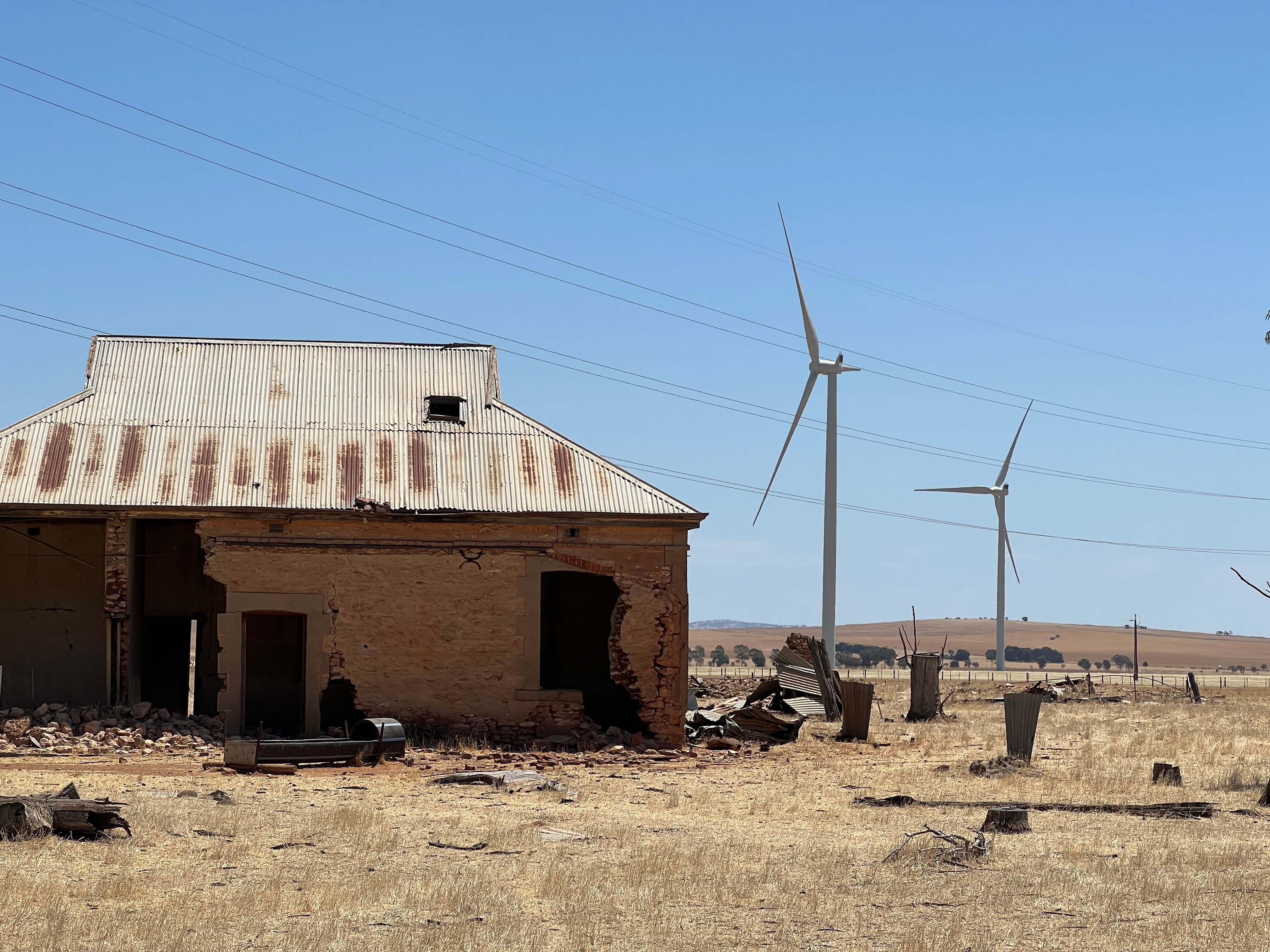 An old, disused farmhouse with wind turbines and transmission lines in the background