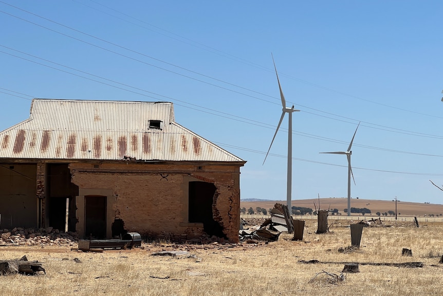Old, disused farmhouse in the foreground with two giant wind turbines in the background