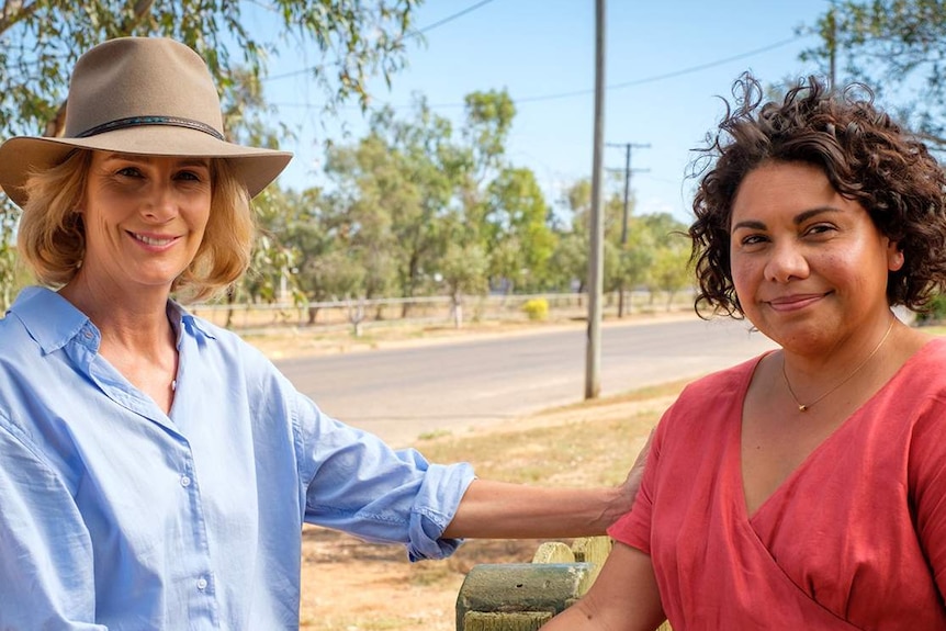 Two women shake hands at the front fence of a house in Winton