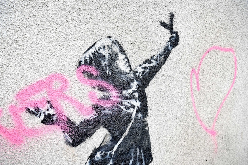 A view of a mural by Bansky which has been vandalised with pink spray paint.
