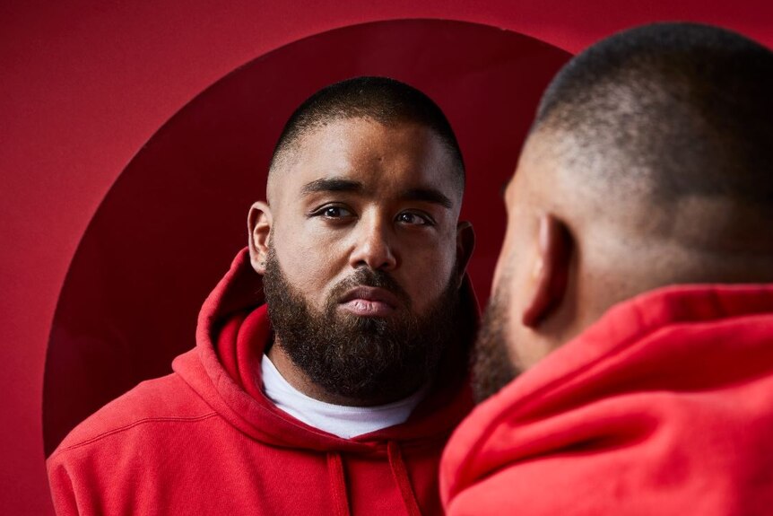 Adelaide musician Adrian Eagle wearing a red hooded jumper and looking into a mirror