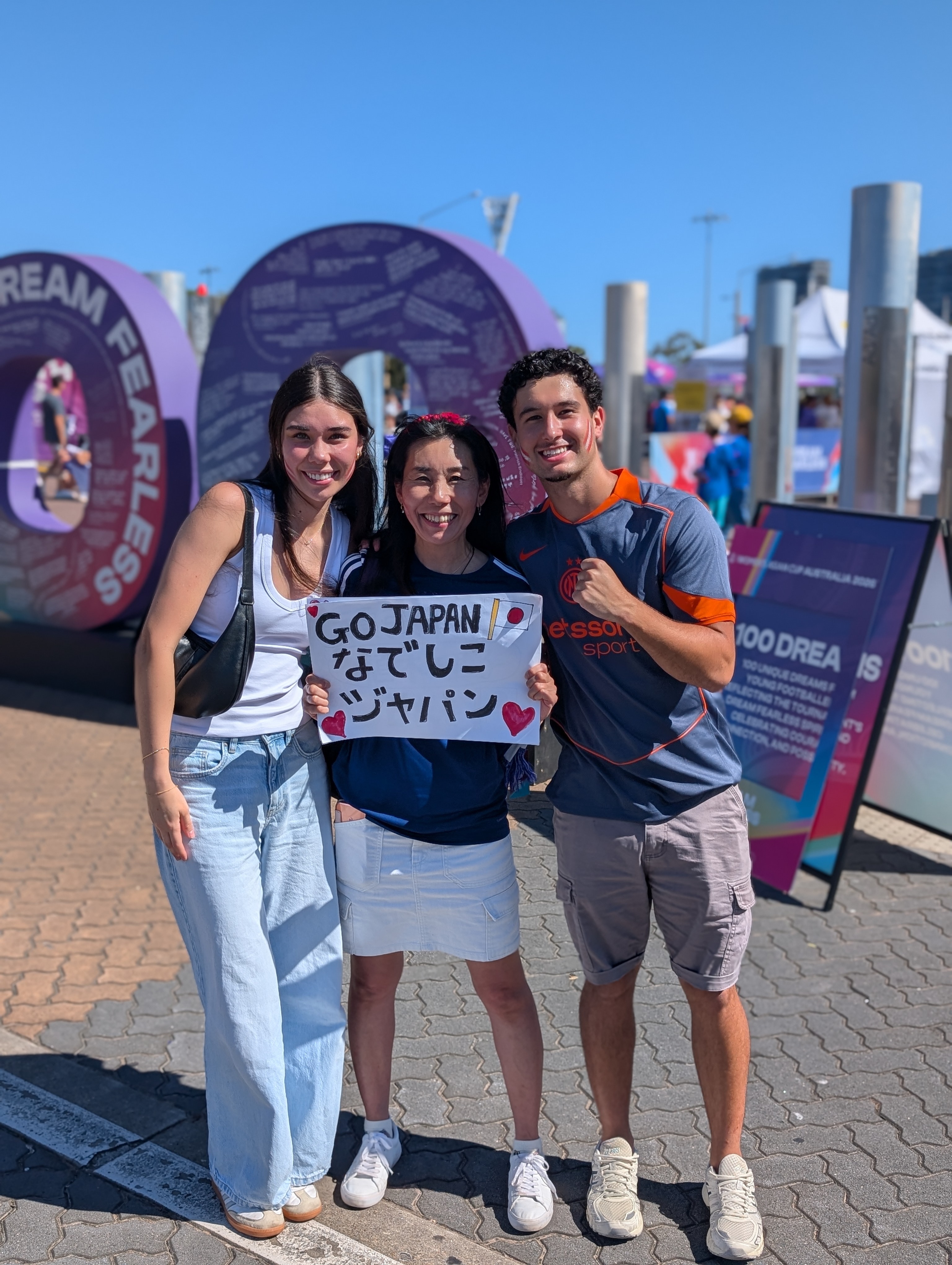 Three people stand and smile holding a Japan sign.