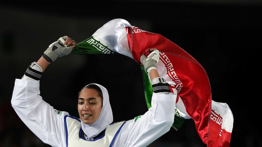 A woman wearing a headscard waves the Iranian flag while wearing a Rio 2016 vest.
