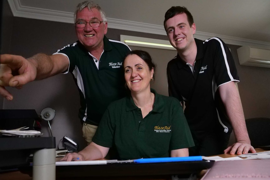 Three BlazeAid workers in an office, smiling while looking at a computer screen.