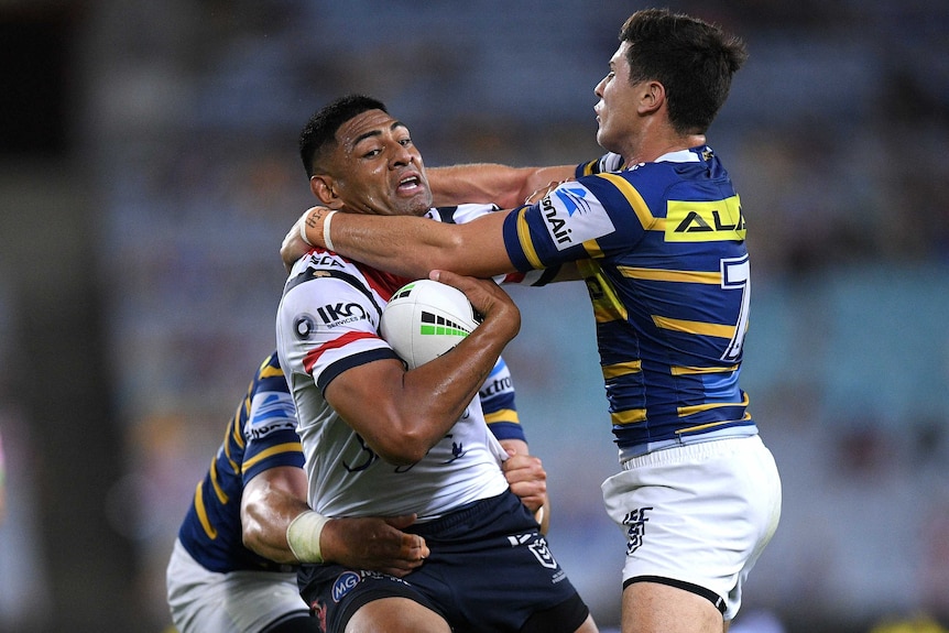 Daniel Tupou is tackled around the neck by Mitchell Moses while holding the ball under his right arm.