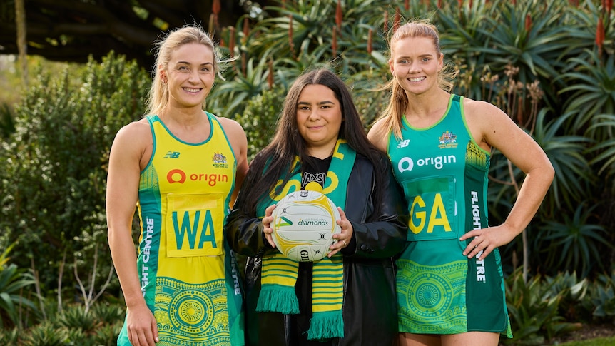 Two Australian netball players wearing the team uniform with the designer of the uniforms standing between them.