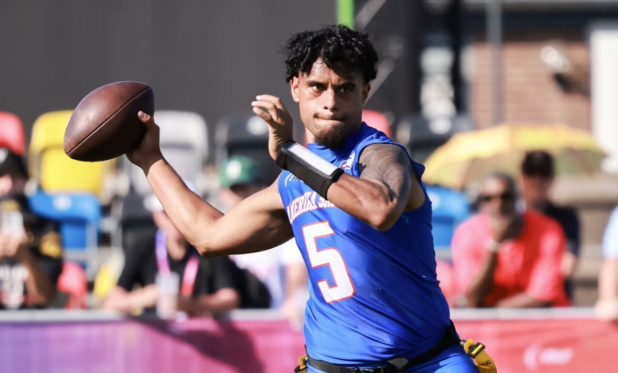 YoungSamoan man draws his hand back holding an American football ball in his hand as he goes to throw wearing blue uniform top