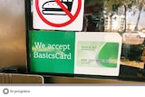 A large green coloured sign on a shop front which reads "We accept BasicsCard"