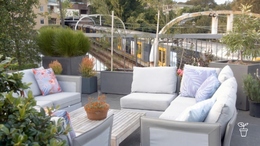 Rooftop garden with couches and potted plants and train going past in background