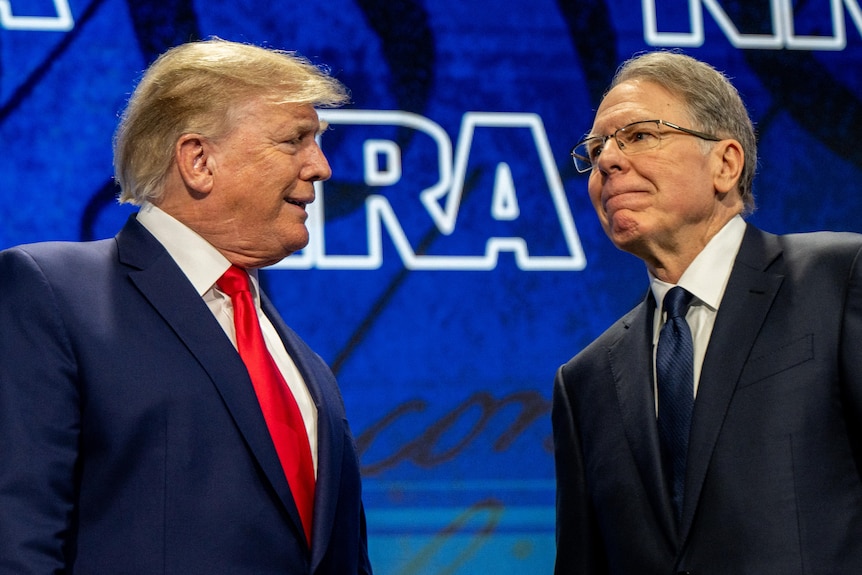 Donald Trump wears a suit and tie. He's smilnig at another man wearing a suit and tie.