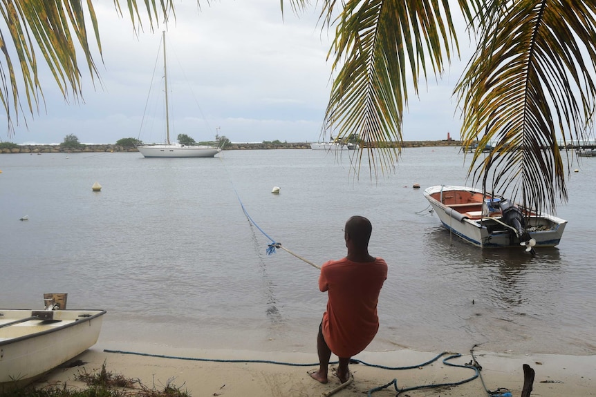 A man pulls a boat from the water with rope.