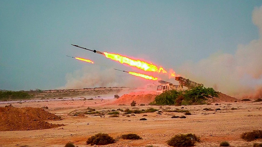Three missiles are launched off a truck in arid landscape
